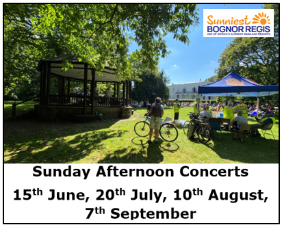 Crowds relax on grass in a sunny park while listening to a live band on a bandstand, with event tents and trees in the background.