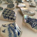 Close-up of blue and white ceramic shards with intricate patterns and glossy surfaces on a white background.