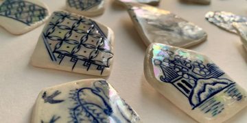 Close-up of blue and white ceramic shards with intricate patterns and glossy surfaces on a white background.