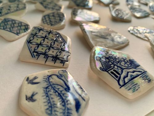 Close-up of blue and white ceramic shards with intricate patterns and glossy surfaces on a white background.
