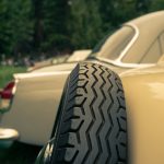 Close-up of a classic car’s spare tire mounted on the side, with another vintage car in the background.