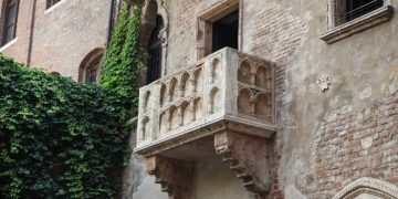 Stone balcony with arches on an old brick building, partially covered by green ivy.