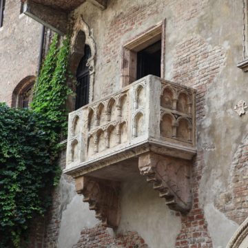 Stone balcony with arches on an old brick building, partially covered by green ivy.