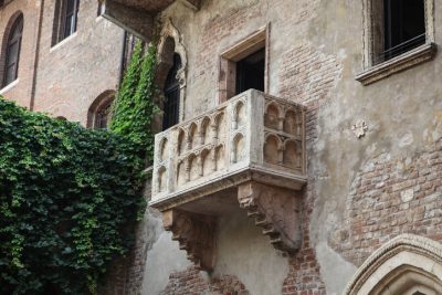 Stone balcony with arches on an old brick building, partially covered by green ivy.